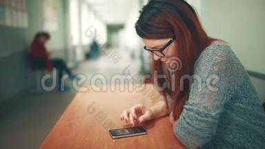 女大学生在大学学院的智能手机上看作业时做笔记。 坐着的女人